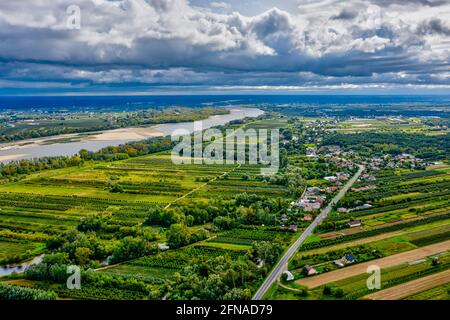 Landschaftlich reizvolle Landschaft, Dorf an gerader Straße und fernem Fluss unter launisch bewölktem Himmel Stockfoto