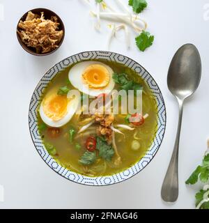 Flaches Lay einer vegetarischen indonesischen Suppe, traditionell mit Huhn namens soto ayam auf weißem Hintergrund mit gekochtem Ei und gebratenen Zwiebeln, Kopie Stockfoto