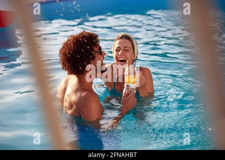 Junges multiethnisches Paar, das im Freibad mit lachend Säfte in ihren Händen Stockfoto