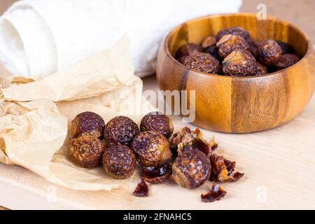 Braune trockene Seifennüsse (Soapberries, Sapindus Mukorossi) in einer Holzschale für Bio-Wäsche und sanfte natürliche Hautpflege auf hellem Hintergrund. Stockfoto