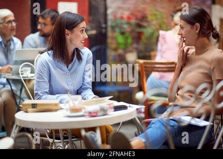 Zwei Studentinnen, die im Garten der Bar bei einem Drink klatschen. Freizeit, Bar, Freundschaft, Outdoor Stockfoto