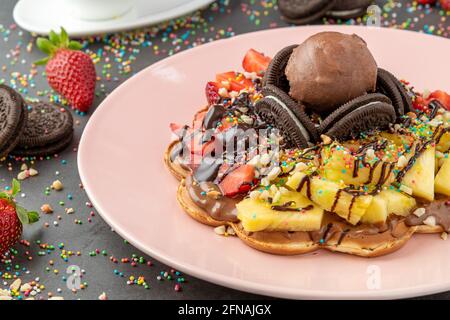 Herzwaffel mit Ananas und Erdbeere mit Gummy Candy und Eis darauf. Stockfoto