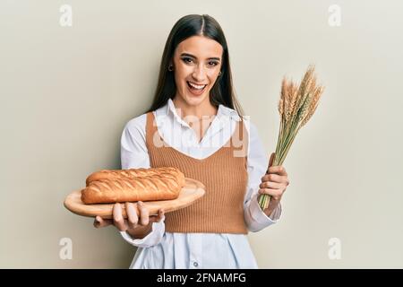 Schöne Brünette junge Frau hält hausgemachtes Brot und Spike Weizen lächeln und lachen hart aus laut, weil lustig verrückt Witz. Stockfoto