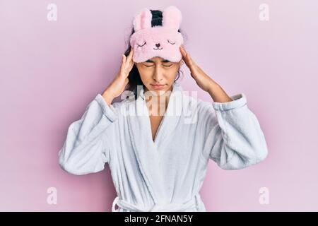 Hispanic Teenager Mädchen mit Zahnspangen tragen Schlafmaske und Robe leiden unter Kopfschmerzen verzweifelt und gestresst, weil Schmerzen und Migräne. Hände Stockfoto