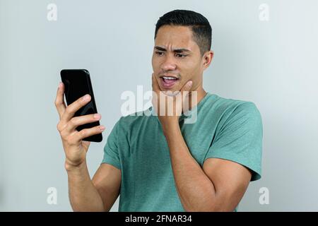 Der 28-jährige brasilianische junge Mann hält und blickt auf das Smartphone mit der Hand auf dem Kinn. Stockfoto