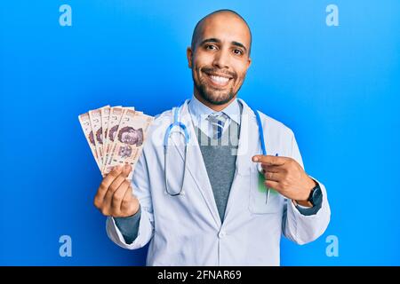 Hispanic erwachsenen Arzt Mann trägt medizinische Uniform hält 500 mexikanische Pesos lächeln glücklich zeigen mit Hand und Finger Stockfoto