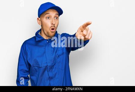 Glatze Mann mit Bart tragen Baumeister Jumpsuit Uniform zeigt mit Finger überrascht voraus, offenen Mund erstaunt Ausdruck, etwas auf der Vorderseite Stockfoto