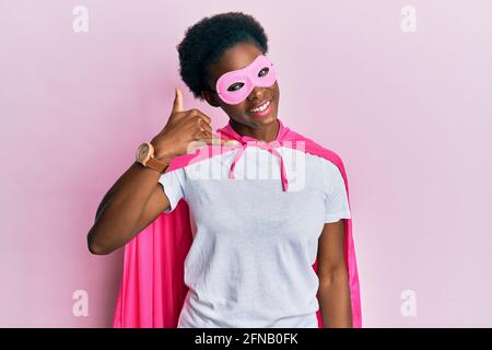 Junge afroamerikanische Mädchen trägt Superhelden-Maske und Cape Kostüm lächelnd dabei Telefongesten mit Hand und Fingern wie am Telefon sprechen. c Stockfoto