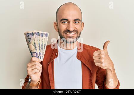 Junger hispanischer Mann, der 5000 japanische Yen-Banknoten hält, lächelt glücklich und positiv, tut vorzüglich und genehmigt das Zeichen Stockfoto