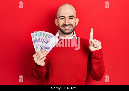 Junger kahler Mann mit ägyptischen Pfund-Banknoten lächelt mit einer Idee oder Frage, die mit dem Finger mit einem glücklichen Gesicht zeigt, Nummer eins Stockfoto