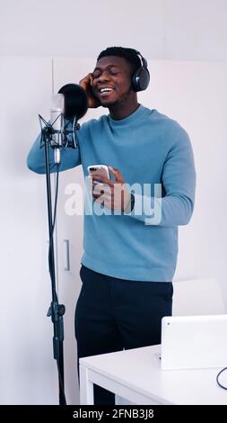 Mann mit Kopfhörern, der in einem Studio ein Lied in ein Mikrofon singt - Aufnahme . Hochwertige Fotos Stockfoto