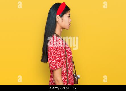 Schöne junge asiatische Frau trägt Kleid und Vintage-Kamera suchen zur Seite, entspannen Profil Pose mit natürlichen Gesicht mit selbstbewussten Lächeln. Stockfoto