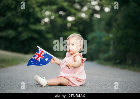 Niedlich liebenswert kaukasischen Baby Mädchen winkt australische Flagge. Lächelndes Kind, das auf der Straße im Park sitzt und den Australia Day feiert. Feiern Stockfoto