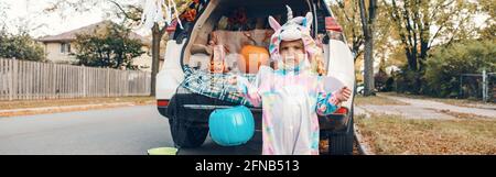 Trick or Trunk. Traurig verärgert Baby im Einhorn Kostüm feiert Halloween im Kofferraum des Autos. Nettes Kleinkind Vorbereitung für Oktober Urlaub im Freien. Stockfoto