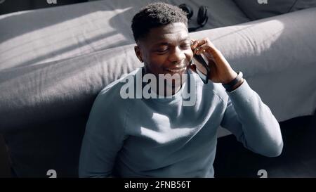 Afroamerikanischer Mann, der auf dem Boden sitzt und mit jemandem am Telefon spricht. Hochwertige Fotos Stockfoto