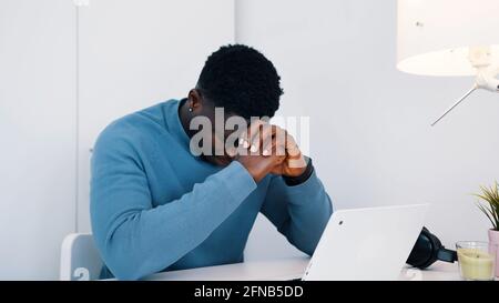 Afroamerikanischer schwarzer Mann sitzt am Tisch vor einem Laptop und arbeitet. Gestresster Mann, der an seinem Laptop arbeitete. Hochwertige Fotos Stockfoto