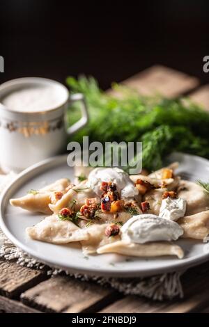 Gefülltes Pirohy-Gericht mit gebratenem Speck, frischem Dill, Sauerrahm und einer Tasse Milch. Stockfoto