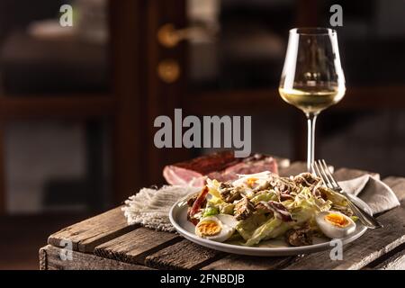 Caesar Salat mit Croutons und Ei serviert auf einem rustikalen Holz mit einem Glas Weißwein. Stockfoto