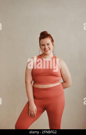 Frau im Fitnessbereich steht nach dem Training. Eine Frau in der Größe „Fit Plus“, die die Kamera anschaut und lächelt. Stockfoto