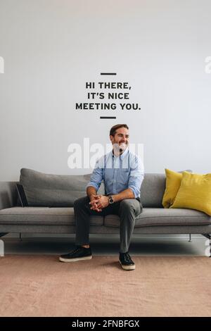 Selbstbewusster Geschäftsmann, der auf dem Sofa sitzt und wegschaut. Glücklicher Manager in der Lobby mit Blick auf die Gäste. Stockfoto
