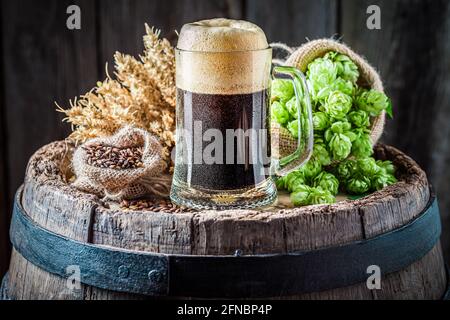 Pint dunkles Bier mit großem Schaum. Brauindustrie. Dunkles Bier auf Holzfass. Stockfoto