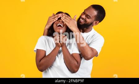 Glücklicher schwarzer Mann, der seine Frau überrascht und die Augen bedeckt Stockfoto