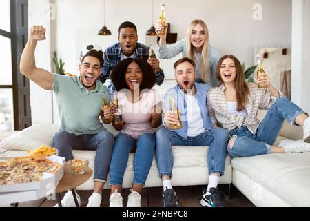 Eine Gruppe junger Freunde mit Snacks und Bier, die Fußballspiele im Fernsehen anschauen und die Lieblingsmannschaft zu Hause anfeuern Stockfoto