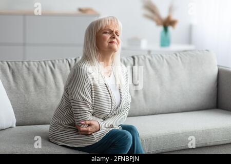Reife Frau, die an Magenschmerzen leidet und ihren Bauch berührt Stockfoto