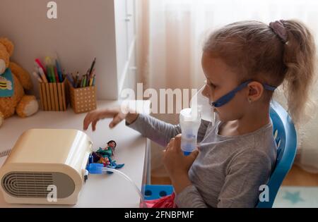 Kleines Mädchen mit einer Inhalationsmaske am Tisch sitzend Stockfoto