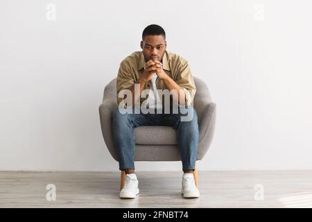 Nachdenklicher Afrikanischer Mann, Der Im Stuhl Auf Grauem Hintergrund Sitzt Stockfoto