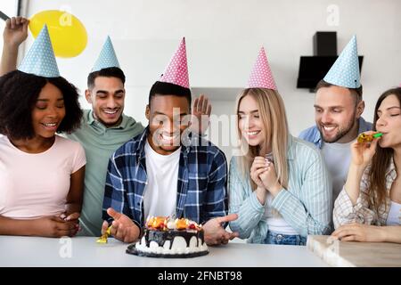 Eine Gruppe junger, vielfältiger Freunde gratulierte dem schwarzen Mann zu seinem Geburtstag, präsentierte festliche Kuchen und trug Partyhüte Stockfoto