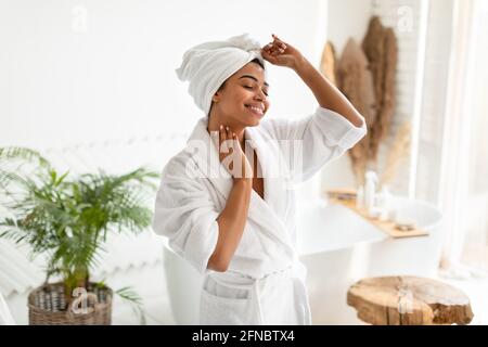 Glückliche Afrikanisch-Amerikanische Frau, Die Im Badezimmer Weißen Bademantel Trägt Stockfoto