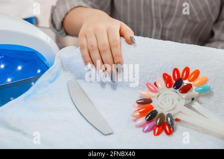 Frau mit künstlichen Acryl-Nägeln nimmt während der Maniküre neue Polierfarbe auf. Maniküre Prozess im Schönheitssalon auf weißem Handtuch. Hygiene Stockfoto