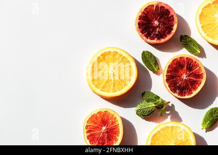 Rot-gelb-orange Scheiben mit grünen Minzblättern auf weißem Hintergrund, scharfe Schatten. Draufsicht, Kopierbereich Stockfoto