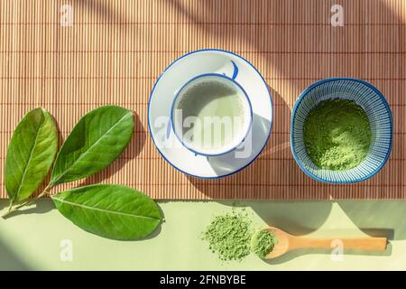 Grüner Matcha-Tee in einer weißen Tasse, Teepulver und Holzlöffel auf Bambusserviette, Draufsicht. Gesundes Getränk. Flach liegend Stockfoto