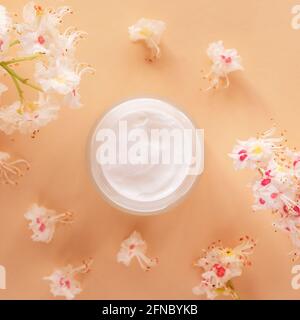 Weißes cremefarbenes Glas und Kastanienblüten auf beigem Hintergrund. Natürliche Bio-Kosmetik-Konzept. Draufsicht, flach liegend Stockfoto