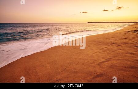Tropischer Sandstrand mit Bewegung verschwommen Wellen bei Sonnenuntergang, Farbtonung angewendet. Stockfoto