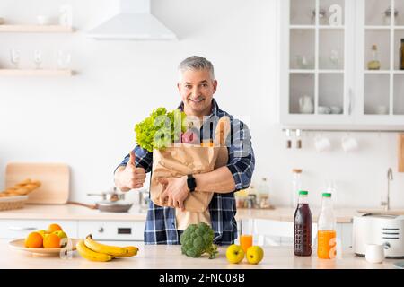 Glücklicher älterer Mann, der den Daumen hochhielt und den Papierbeutel voll hielt Von gesundem Gemüse und Lebensmitteln Stockfoto