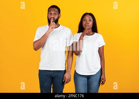 Schwarzes Paar, das Finger auf die Lippen stampft und ein Zeichen für die Stille macht Stockfoto