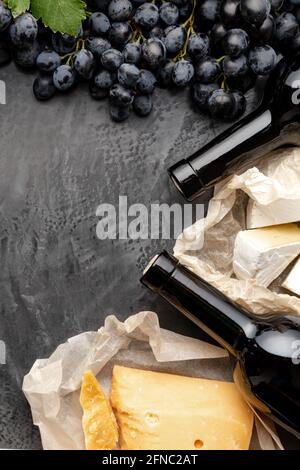 Rotwein Flasche Käse Trauben. Jahrgang Stillleben Weinzusammensetzung mit gereiftem Käse Camembert Kräuter, Trauben. Abendessen im Restaurant, Weinprobe im Dunkeln Stockfoto