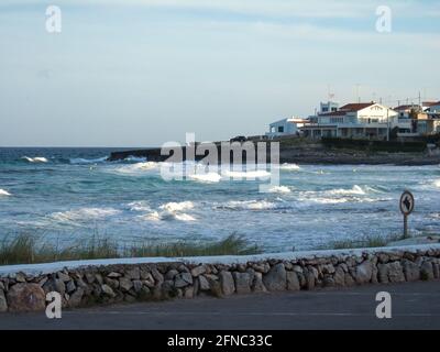 Blick auf den Strand von Punta Prima. Bei sonnigem, warmem Wetter waschen einige weiße Wellen das Meerwasser an der Küste. Im Hintergrund sieht man Strandhäuser Stockfoto