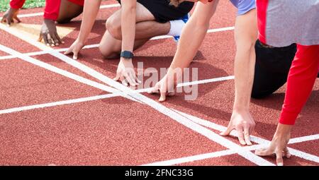 High School-Jungen führen Laufstrecken und Feldläufer an der Startlinie durch, die bereit sind, ein Sprintrennen in den Spuren auf einer roten Strecke zu starten. Stockfoto