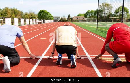 Rückansicht von drei männlichen High School Sprinterläufern, die beim Training auf der Strecke an der Startlinie bereit waren. Stockfoto