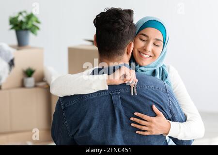 Emotionale junge Dame in Hijab mit Schlüssel umarmt ihren Mann Stockfoto