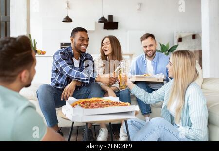 Eine Gruppe verschiedener Freunde, die Party machen, Pizza trinken, Bier trinken, Toast machen, etwas zu Hause feiern Stockfoto