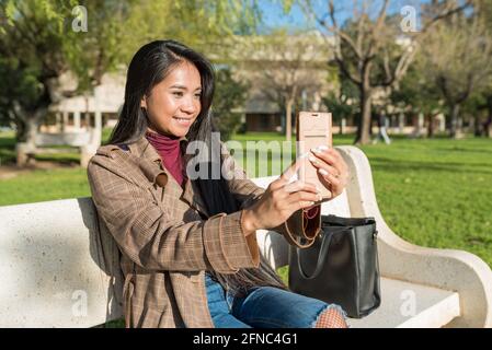 Junge asiatische Frau mit einem Videoanruf auf einem sitzen parkbank Stockfoto