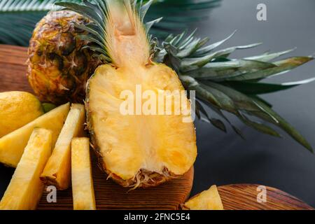 Ananas auf Schneidebrett. Frische, süße, halbgeschnittene Ananas und ganze Ananasfrüchte. Sommer Obst in Scheiben geschnitten Ananas Kochvorgang in der Küche auf dunkel Stockfoto