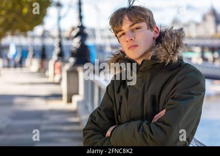 Junge Erwachsene männliche junge Teenager draußen in der Sonne trägt ein kapuzenparka in einer Stadt Stockfoto