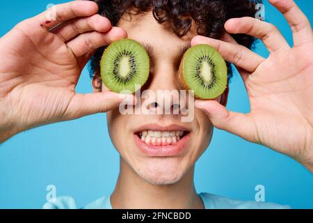 Mann mit lockigem Haar, der Kiwi in der Nähe des Klassengesichts hält Emotionen Stockfoto