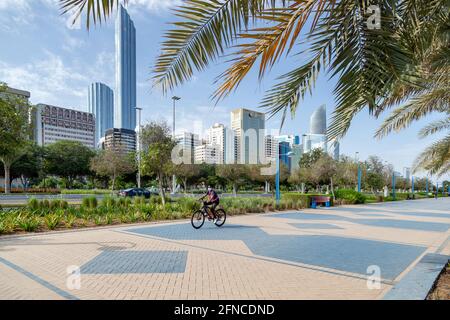 ABU DHABI, VAE - 30. APRIL 2021: Mann fährt morgens auf der Abu Dhabi Corniche mit modernem Stadtbild im Hintergrund. Aktiver Lebensstil. Stockfoto